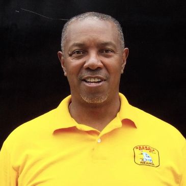 Man wearing a bright yellow polo shirt with an embroidered logo, smiling against a black background.