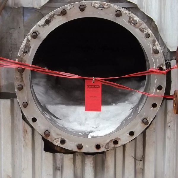 Large industrial pipe with a red barricade warning tag and tape across its opening.