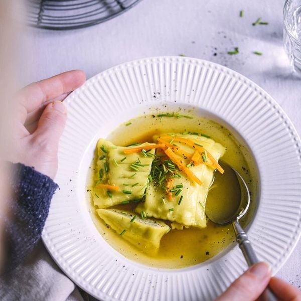 Plate of ravioli in broth garnished with herbs and carrots.