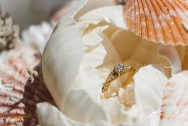 Gold engagement ring inside white flower surrounded by seashells.