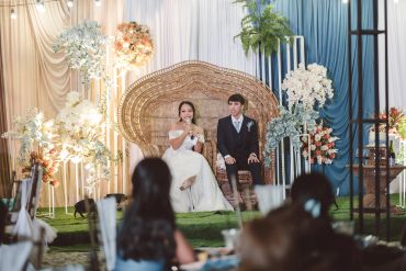 Bride and groom sitting on a decorative chair during their wedding.