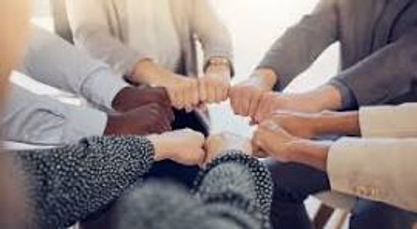 A group of people joining fists in a circle, symbolizing unity and teamwork.