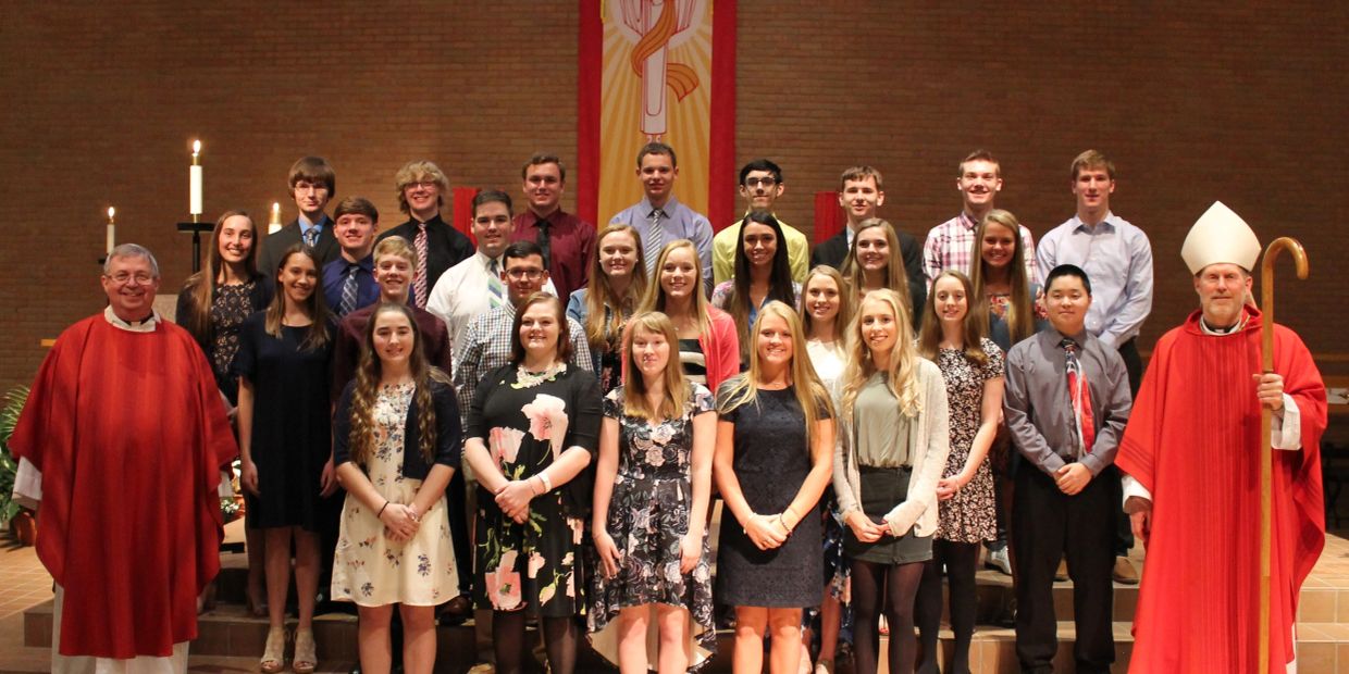 Group of young people and clergy in red robes posing in a church.