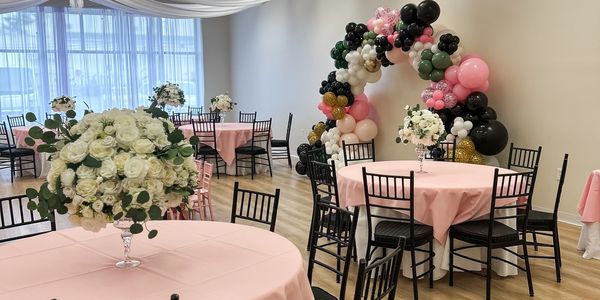 Elegant party setup with pastel pink tablecloths and a colorful balloon arch.