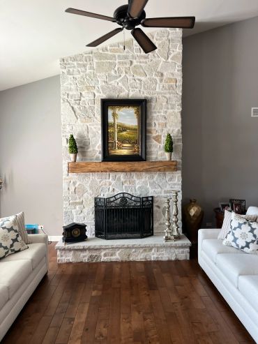 Cozy living room with a stone fireplace, wooden mantle, and neutral-toned sofas.