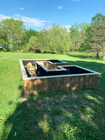 Wooden raised garden bed with multiple compartments on green lawn.