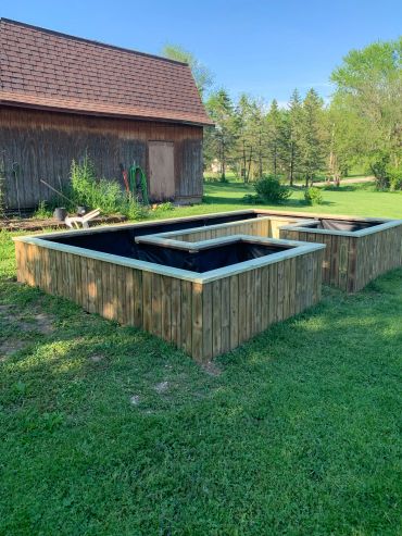 Wooden raised garden beds near a rustic barn in a grassy yard.