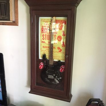 Black electric guitar displayed in a wooden wall-mounted glass cabinet.
