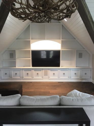 Modern living room with white built-in shelves and a mounted TV under a vaulted ceiling.