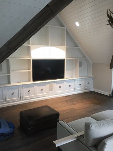 Cozy attic living room with built-in white shelves and a TV.