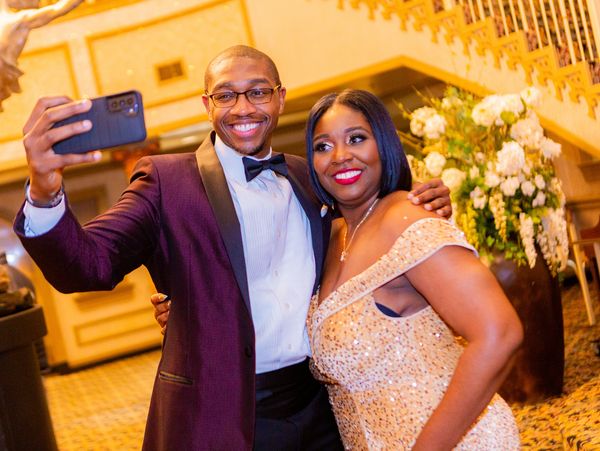 A well-dressed couple takes a joyful selfie at an elegant event.