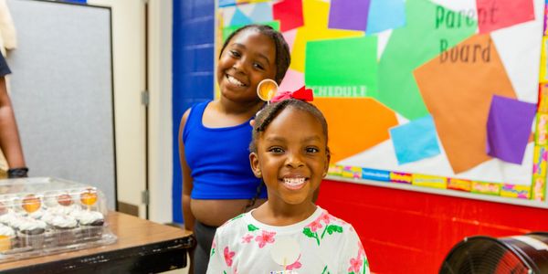 Two joyful girls smiling in a colorful classroom setting.