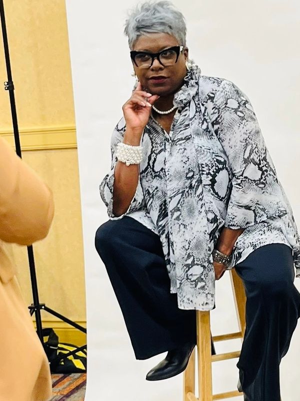 Woman in snake print blouse sitting on a stool.