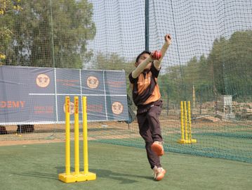 A young cricket player bowling during practice in a netted area.