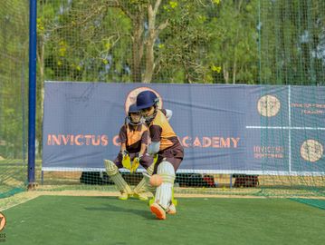 Young cricket players practicing batting and wicketkeeping on a green field.