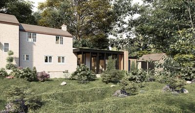 Stone house with modern glass extension surrounded by greenery and trees.