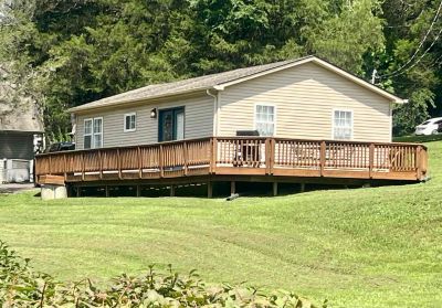 Single-story beige house with wooden deck in a grassy area.