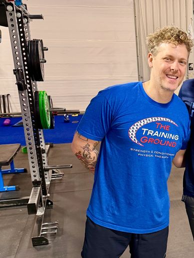 Man smiling in a gym wearing a blue Training Ground t-shirt.