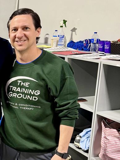 Man in green sweatshirt standing in front of shelves with various items.