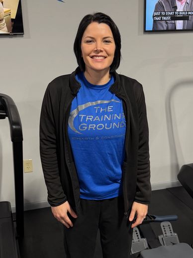 Smiling woman in gym attire standing between exercise machines.