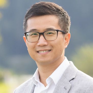 Smiling man wearing glasses and a light gray blazer.