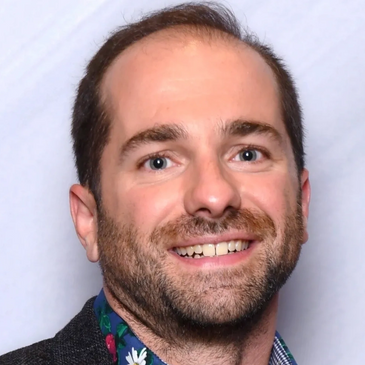 Portrait of a smiling man with a beard and floral shirt collar.