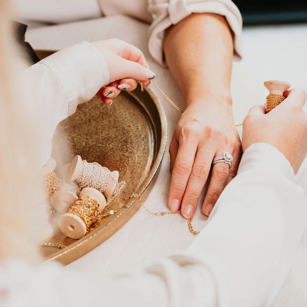 Two people working with gold chains and spools, focusing on hands and jewelry.
