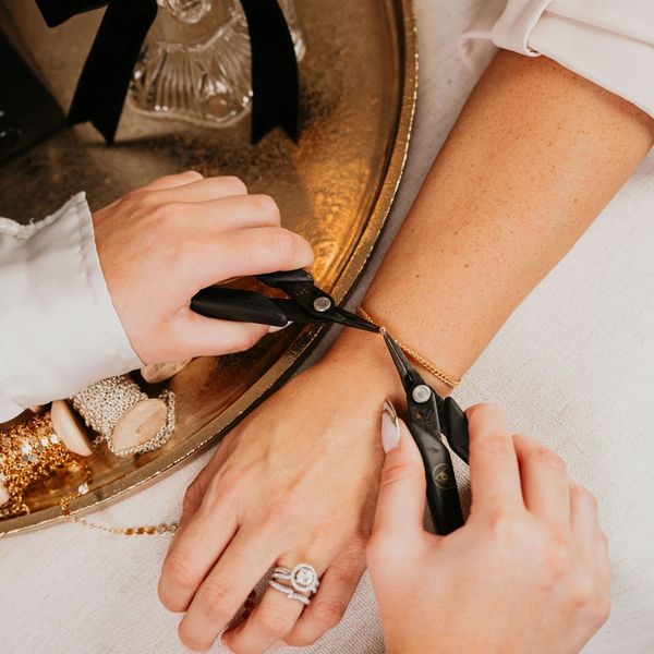 Hands using pliers to fasten a delicate gold bracelet on a wrist.
