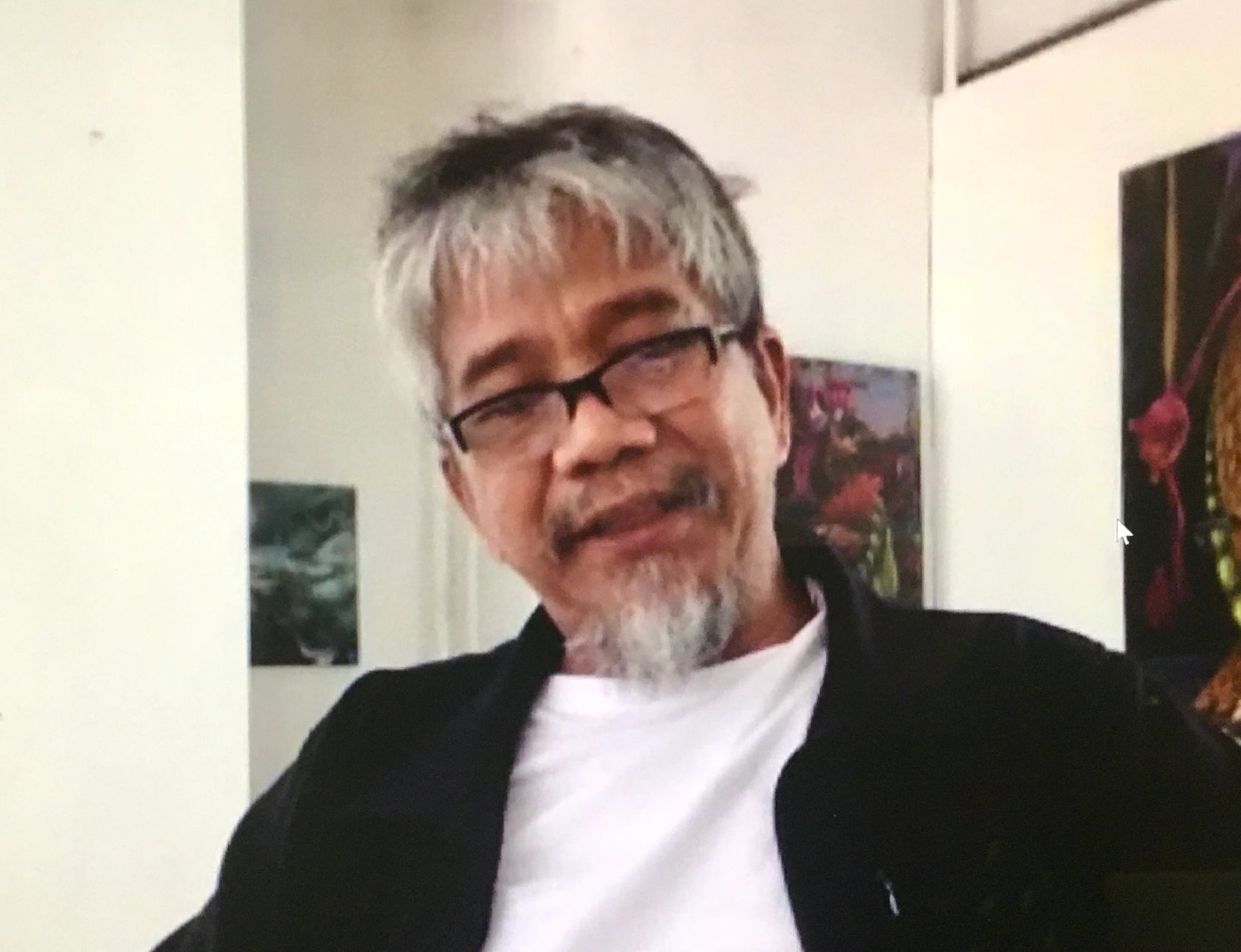 An older man with gray hair and glasses smiles gently in an indoor setting.
