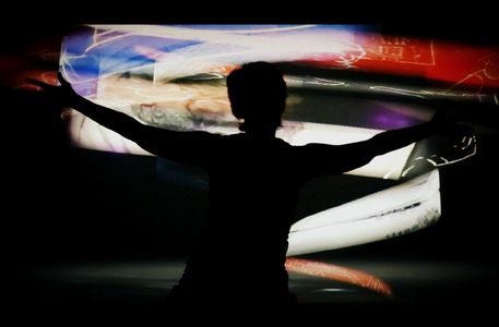 Silhouette of a person with arms outstretched against colorful abstract light projections.