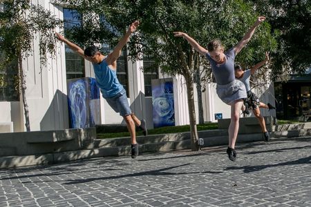 Three dancers leap gracefully outdoors on a sunny day.