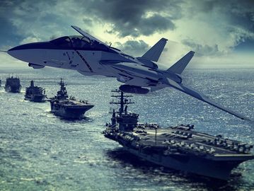 A fighter jet flying over a fleet of aircraft carriers in the ocean.