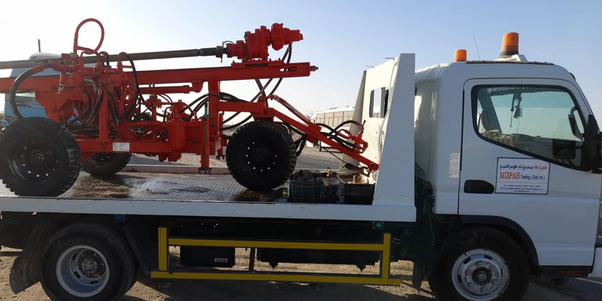 White flatbed truck carrying a red heavy-duty machinery under clear sky.