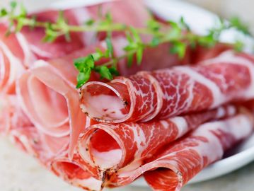 Thinly sliced cured meat rolls garnished with fresh herbs.