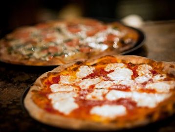 Two freshly baked pizzas with melted cheese on a wooden table.