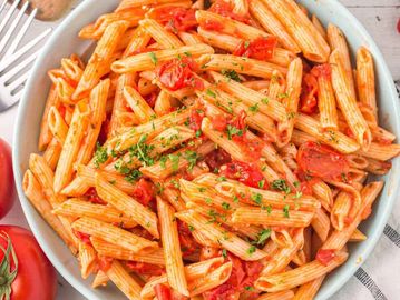 Plate of penne pasta with tomato sauce and herbs.