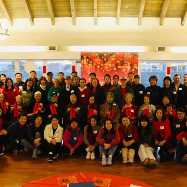 Group photo of diverse people celebrating indoors with red decorations.