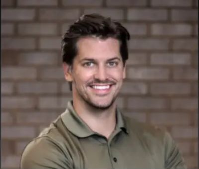 Smiling man with folded arms in front of a brick wall.