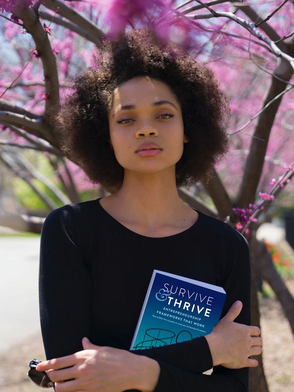 A woman holding the book Survive & Thrive. photo credit: Thought Catalog on Unsplash