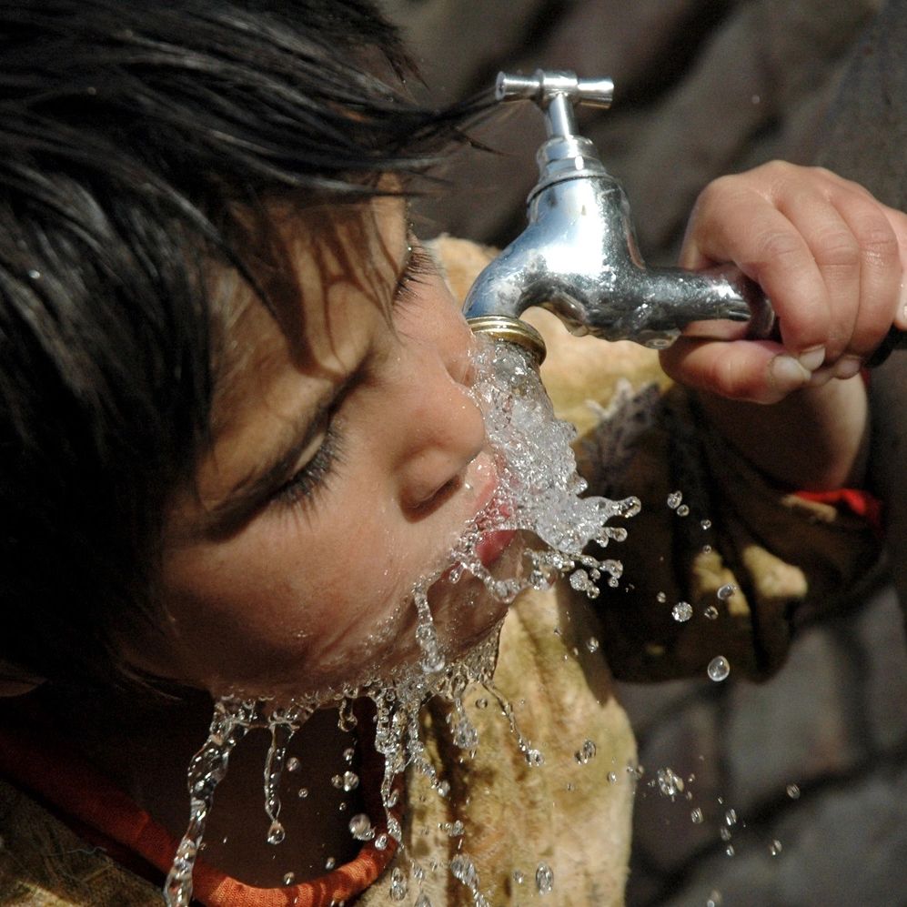 A young child drinking from a water tap.
