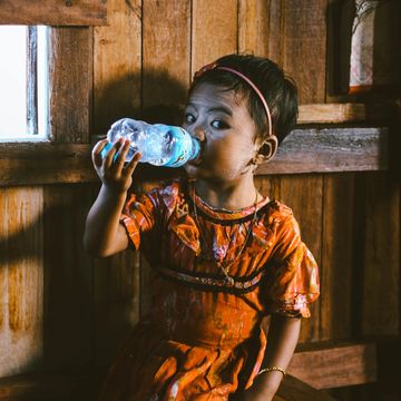 A small girl drinking water from a plastic bottle. photo credit: Chinh Le Duc on Unsplash