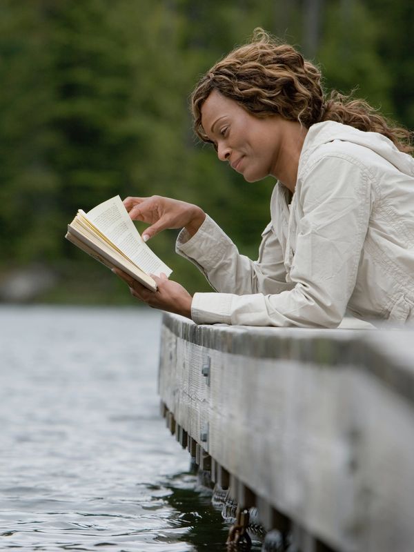 A woman reading a book on the dock of a lake. photo credit: Getty Images on Unsplash