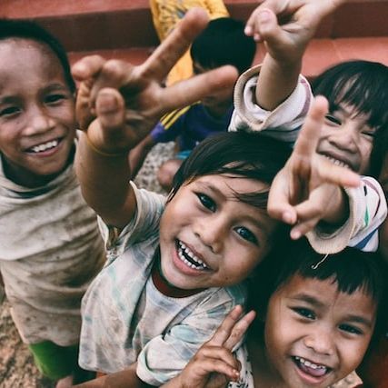 Smiling faces of children who are showing the peace sign. photo credit: Larm Rmah on Unsplash