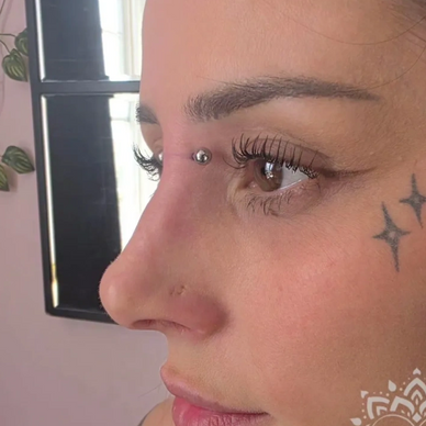 Close-up of a woman's face with a nose piercing and star tattoos near her eye.