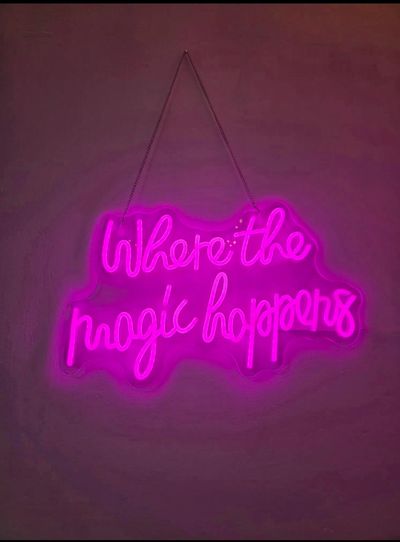 Pink neon sign reading 'Where the magic happens' glowing on a dark wall.