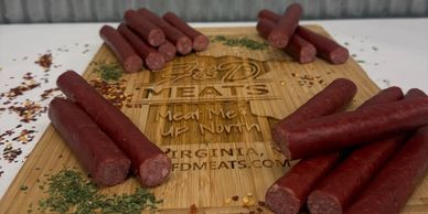 Various meat sticks arranged on a branded wooden cutting board with herbs and spices.