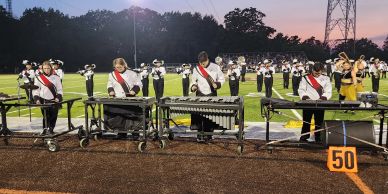 High school marching band performing on football field at dusk.