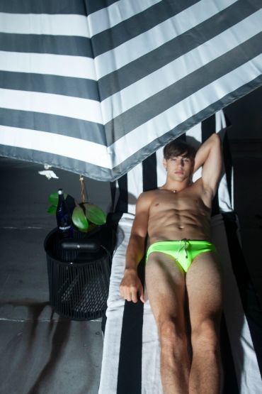 Man in neon green swimwear lounging under a striped umbrella.