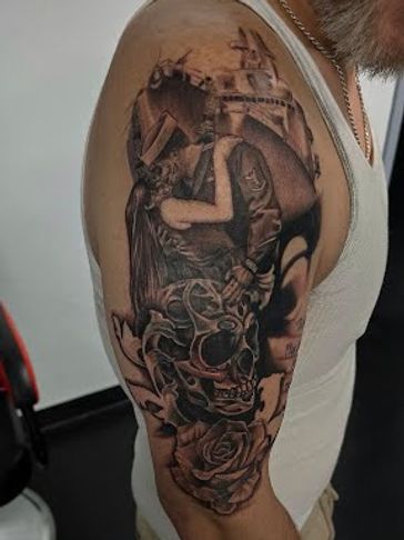 Detailed black and grey tattoo of a kissing couple, skull, and roses on upper arm.
