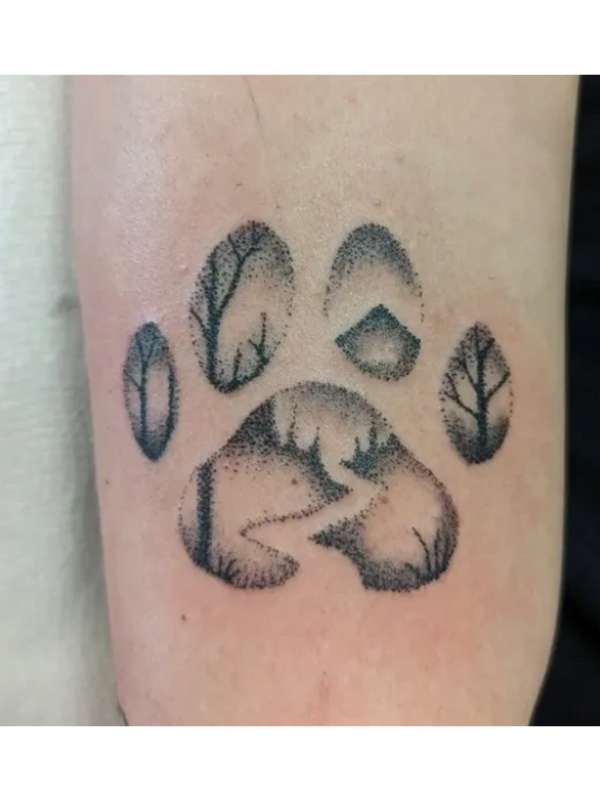 Tattoo of a paw print with tree silhouettes inside each pad.